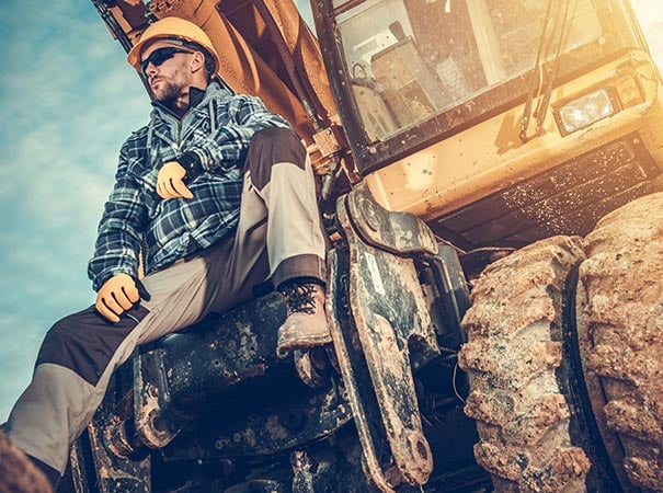 Excavator operator rests against machinery at construction site