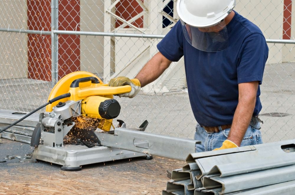 Worker cutting metal with electric saw, powered by generator