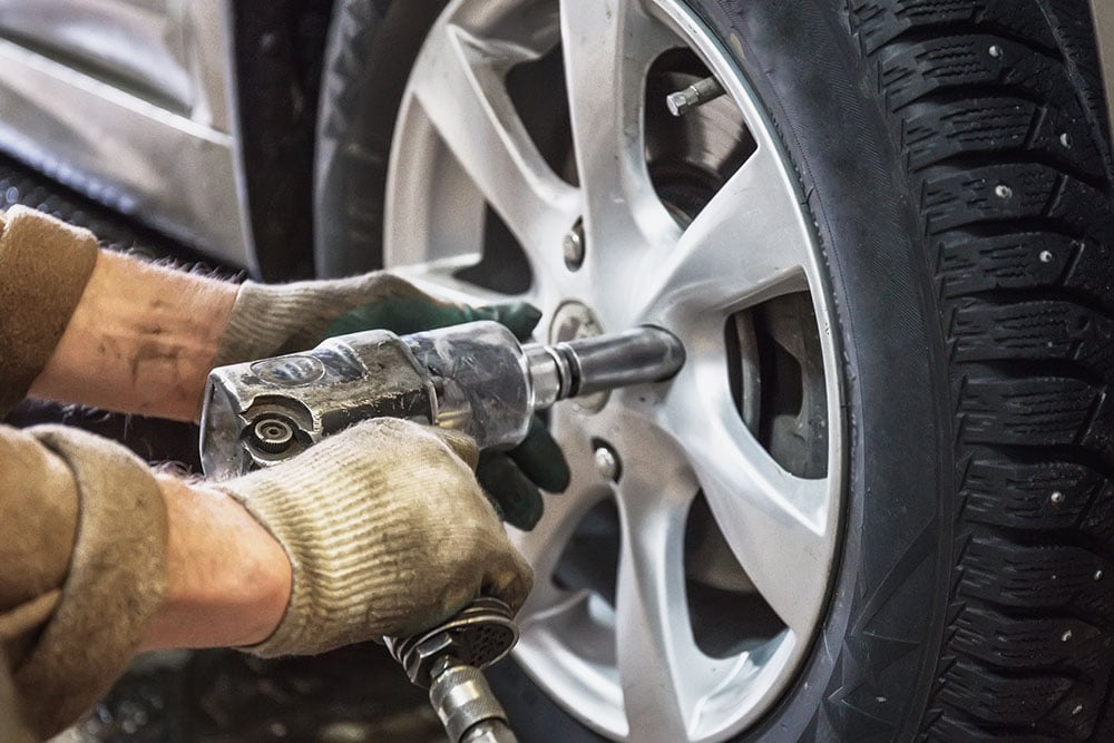 Man's hands using impact wrench on wheel nut