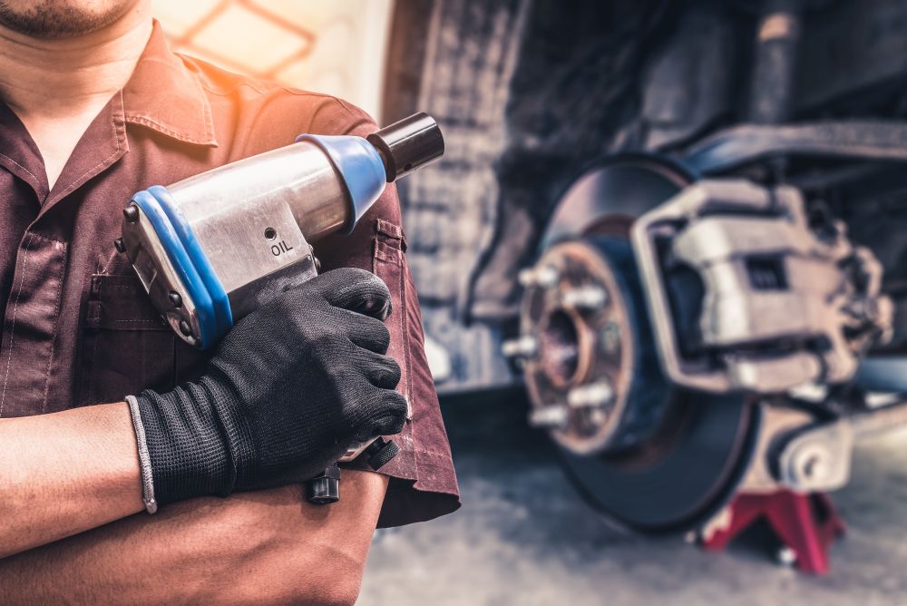 Tough tire service tech holds impact wrench in front of dismantled tire