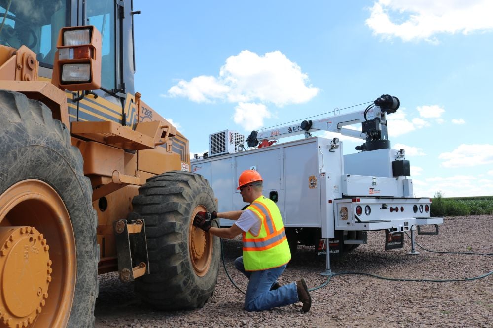 Mechanic fixes machine tire in front of crane truck with VMAC hydraulic compressor