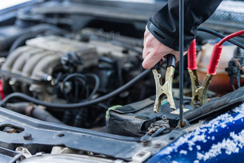 A man connects boosting cables to vehicle engine battery