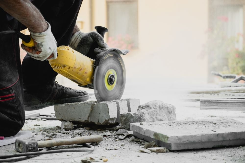 Worker uses power saw to cut into cement